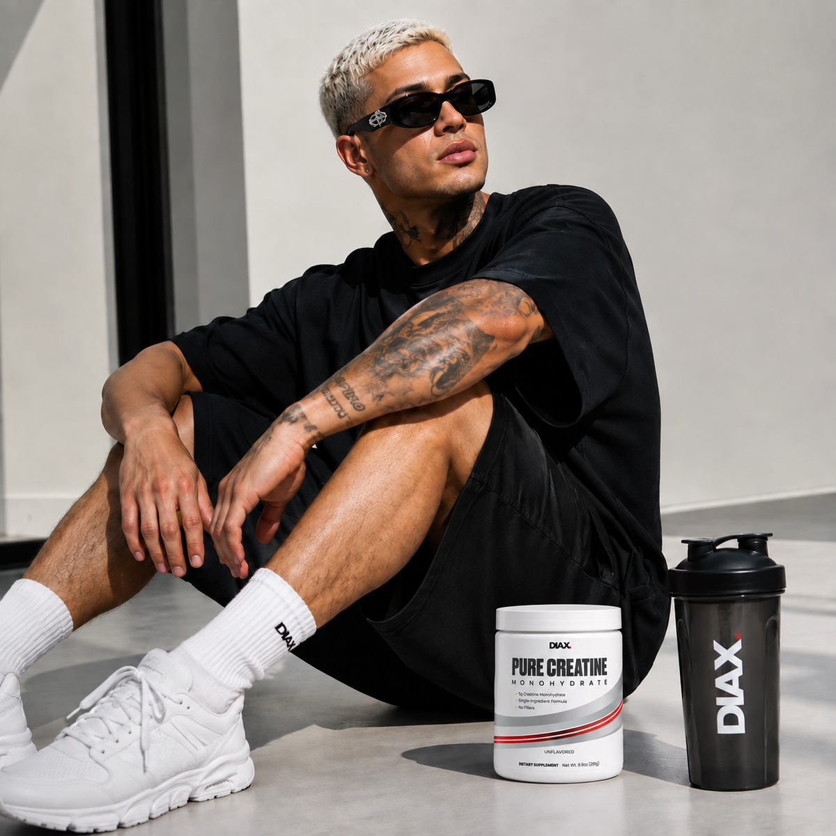 Lifestyle image of an athlete sitting indoors with DIAX Pure Creatine Monohydrate supplement jar and DIAX shaker bottle